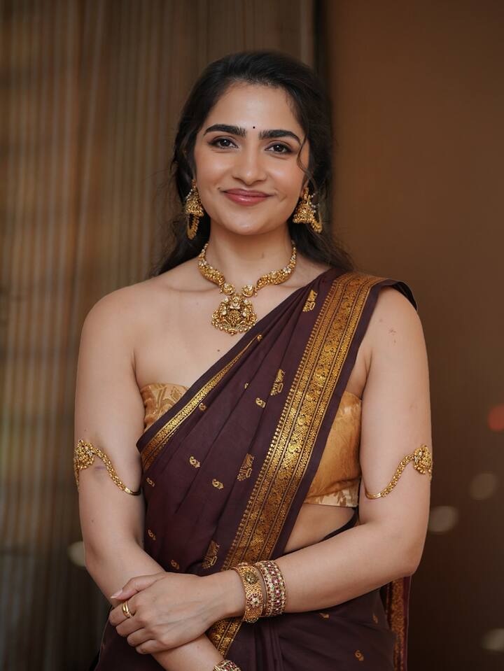 रुक्मिणी ने इस लुक में चॉकलेट रंग की साड़ी पहनी है, जिस पर गोल्डन रंग का खूबसूरत बॉर्डर और बारीक बूटी का काम किया गया है. इस साड़ी को उन्होंने गोल्डन रंग के ऑफ-शोल्डर ब्लाउज के साथ पेयर किया है, जो उनके लुक को स्टाइलिश टच दे रहा है. गले में चौड़ा टेंपल ज्वैलरी हार, कानों में झुमके, हाथों में चूड़ियाँ और कंगन, वहीं गोल्ड के बाज़ूबंद उनके रॉयल लुक को पूरा कर रहे हैं. खुले लहराते बाल और न्यूड टोन मेकअप के साथ रुक्मिणी इस लुक मे बेहद क्लासी और एलीगेंट नजर आ रही है.