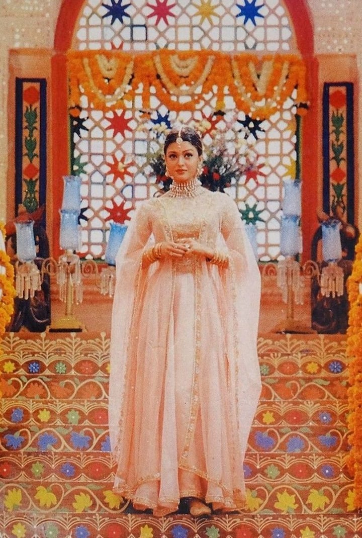 ऐश्वर्या राय के किरदार नंदिनी से बाहर क्लासिक लुक इंस्पिरेशन। फिल्म 'हम दिल दे प्राचीन सनम' के गाने 'आंखों की गुस्ताखियां' में उनका गुलाबी लहंगा खूबसूरती की मिसाल है। फ़्लोरिडा पोटली, दुपट्टा और फ़्लोई सिल्हूट इस पुतले को बेहद ग्रेसफुल तोड़ते हैं। हाई-नेक डिज़ाइन और ट्रेडिशनल जूलरी में रॉयल कंसीलर हैं। यह लुक पूजा या परिवार के साथ भोजन के लिए बिल्कुल प्रभावशाली है।