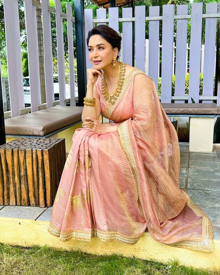 In this look, Madhuri is wearing pink-peach colored tissue saree. This look is perfect for daytime Bhai Dooj functions, where you can wear light colors. The golden zari lines and prints on the saree are giving it a festive touch. She has complemented this saree with traditional heavy golden jewelery like Rani Haar, matching earrings and bangles. If you want to show the magic of traditional gold jewelery with light pastel colors on Bhai Dooj, then definitely adopt this look.
