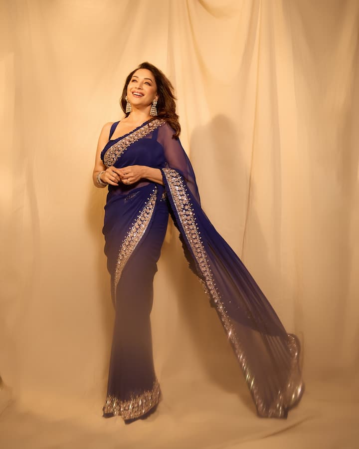 Madhuri is looking very beautiful in this royal blue colored saree. This look is perfect for Bhai Dooj because despite being traditional, it is very modern and classy. The golden thread embroidery on the pallu and border of the saree is giving it a festive touch. She has completed her look with heavy golden earrings and bracelet. This Bhai Dooj, you too can win everyone's heart by wearing a similar dark colored saree with statement jewellery.
