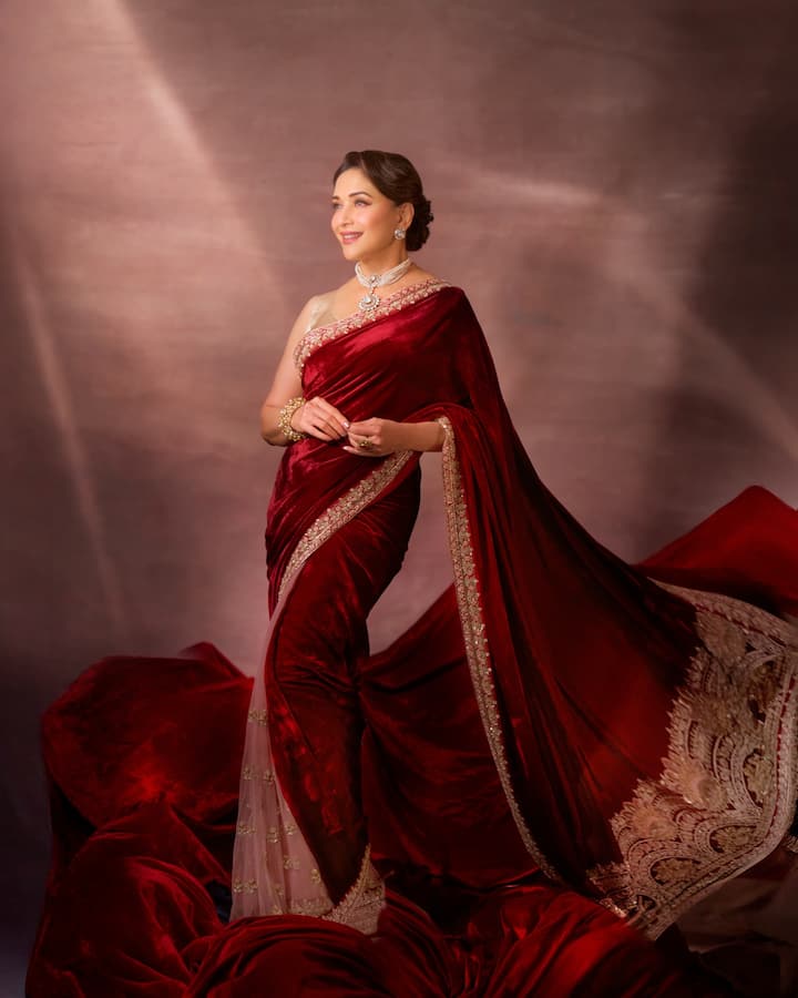 Madhuri is looking very glamorous in this maroon red colored velvet saree. This look is perfect for evening Bhai Dooj function or any special party. The velvet fabric of the saree and the heavy golden gota-patti embroidery done on the pallu are giving it a royal winter-festive look. She paired this rich saree with heavy pearl jewelery like choker necklace and matching bracelet. This combination of velvet and diamond is giving a rich look.