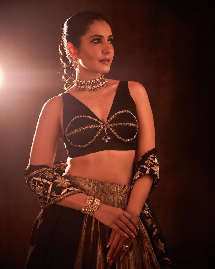 Her makeup is soft and luminous — glowing skin, muted nude lips, kohl-lined eyes with a subtle shimmer, and delicately defined brows. A tiny black bindi adds the perfect finishing touch, grounding the look in classic Indian beauty traditions. Her hair is styled in a sleek, pulled-back bun — clean, regal, and powerfully refined.