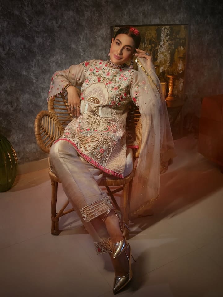 इस तस्वीर मे पवित्रा ने हल्के बेज रंग का एक ट्रांसपेरेंट फैब्रिक वाला अंगरखा स्टाइल का कुर्ता पहना है. इस कुर्ते पर सिल्क के धागों और ज़री से फ्लोरल एम्ब्रॉइडरी की गई है. कुर्ते की स्लीव्स बेल-शेप की हैं, जिन पर काम किया गया है. उन्होंने इसे मैचिंग शाइनी फैब्रिक के ट्राउज़र्स के साथ पेयर किया है. एक्सेसरीज़ में उन्होंने नेक चोकर और हाथों में रिंग पहनी हैं. उनका हेयरस्टाइल स्लीक बन है और मेकअप में हेवी आईज़ हैं. इस पूरे लुक को मेटालिक सिल्वर पॉइंटेड हील्स कंप्लीट कर रहे हैं, जो इसे एक हाई-फैशन अपील दे रहा है.