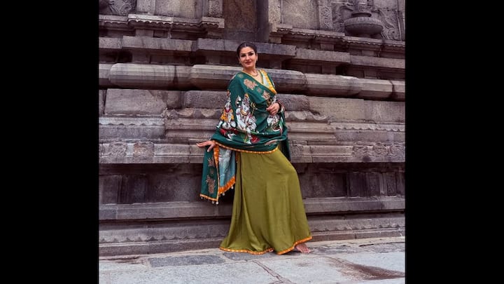 3. Regal Grace In Olive-Green Ensemble: Raveena Tandon stuns in a timeless ethnic look that beautifully blends traditional artistry with understated elegance. The actress dons an olive-green flared skirt paired with a matching blouse, draped gracefully with a rich forest-green shawl adorned with intricate mythological motifs. Styled with minimal accessories and a sleek bun, Raveena lets her outfit do the talking, exuding cultural pride and refined sophistication. This look is a perfect inspiration for anyone seeking a modern yet rooted festive style that celebrates Indian craftsmanship with poise and personality. (Image Source: Instagram/@officialraveenatandon)