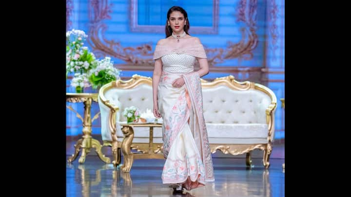 5. ऑफ-शोल्डर ब्लाउज के साथ आइवरी कढ़ाई वाली साड़ी: नाजुक ऑफ-शोल्डर ब्लाउज के साथ जोड़ी गई इस उत्कृष्ट आइवरी साड़ी में अदिति राव हैदरी ने आधुनिक सुंदरता को फिर से परिभाषित किया है। इस पहनावे में बॉर्डर के साथ पेस्टल फूलों की कढ़ाई और नरम गुलाबी लहजे हैं, जो एक स्वप्निल और शाही आकर्षण को दर्शाते हैं। संरचित लेकिन सुंदर सिल्हूट पूरी तरह से उसकी शाही शिष्टता का पूरक है, जो इसे समकालीन दुल्हनों या उत्सव समारोहों के लिए एक असाधारण लुक बनाता है। सुंदर चोकर और मुलायम लहरों के साथ स्टाइल की गई अदिति पारंपरिक शिल्प कौशल को आधुनिक वस्त्र मोड़ के साथ संतुलित करती है। शांत हाथीदांत पैलेट, जटिल कढ़ाई के साथ, उसकी शाश्वत सुंदरता को बढ़ाता है और दिखाता है कि कैसे मामूली ग्लैमर सबसे जोरदार बयान दे सकता है। (छवि स्रोत: इंस्टाग्राम/@अदितिरावहिदरी)