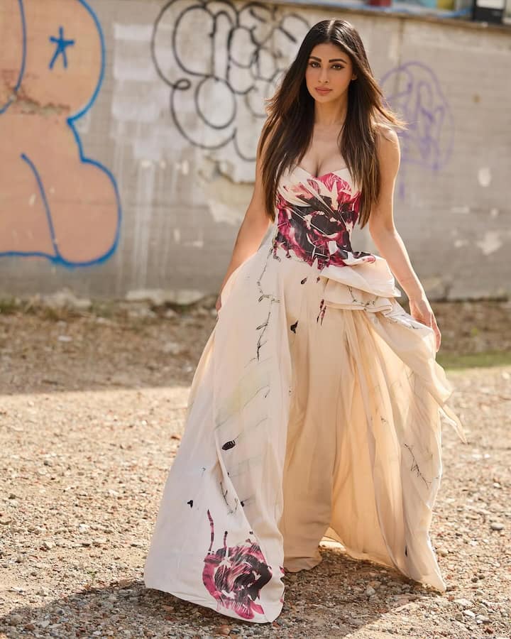 Mouni is wearing a light cream colored gown in this look. It is a strapless gown, which has pink and black print on the upper part. The skirt of the gown is flowy. Mouni has kept her makeup natural.