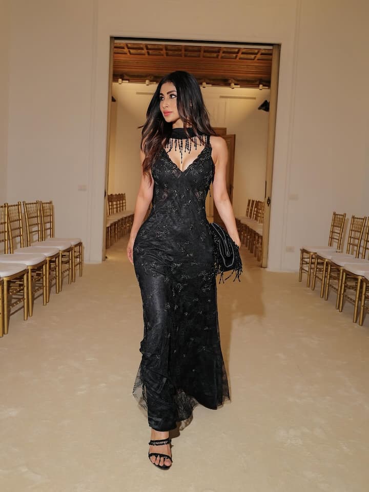 In this look, Mouni is wearing a very beautiful black lace gown. The gown is sleeveless with a V-neckline and a semi fabric choker at the neck. The fitting of the gown is excellent, which is highlighting her figure. She paired it with a black clutch and wore black strappy sandals.
