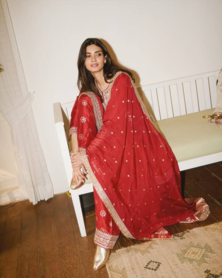Diana has adopted a traditional and elegant look in this picture. She is wearing a beautiful red colored ethnic suit, on which golden zari and gota patti work has been done. The matching dupatta is adding grace to her look. Golden shoes are a perfect match with the outfit. Open hair and nude makeup have made her entire look simple, graceful and perfect.
