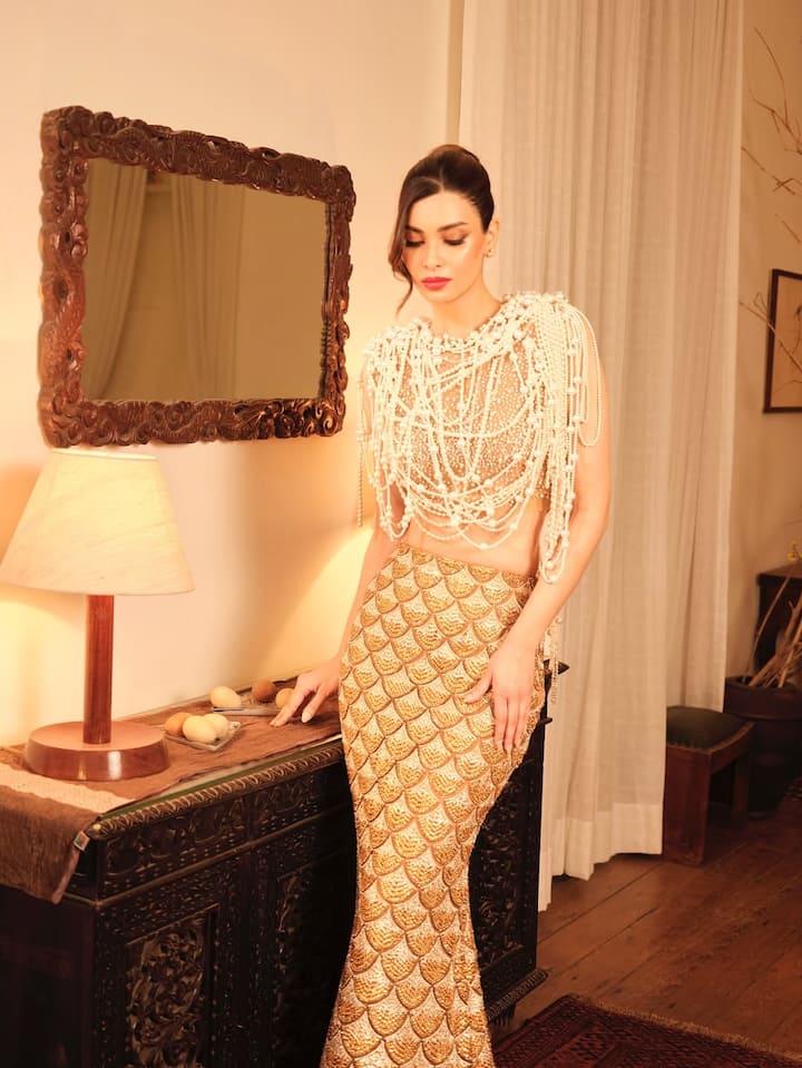 In this look, Diana is seen in a very royal and unique look. She wore a fitted skirt with a golden fish scale pattern, which she paired with a heavy drape-style top studded with pearls. Her minimal makeup, red lips and sleek bun hairstyle are giving a glamorous and classy touch to this look. This look is giving a perfect modern-royal appeal.