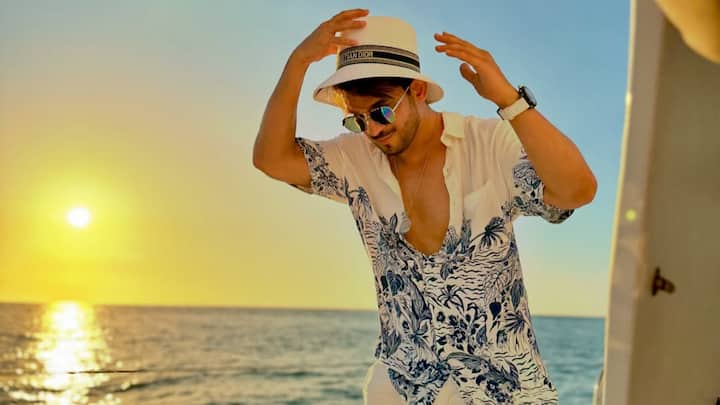 Arjun keeps it effortlessly cool in this white shirt with blue botanical prints paired with white linen trousers. The breezy ensemble, styled with flip-flops and a straw hat, is perfect for seaside brunches or rooftop hangouts. (Image Source: Instagram/ arjunbijlani)