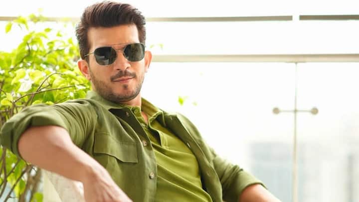 In this earthy-toned look, Arjun layers a light olive shirt jacket over a darker green tee with beige trousers. The aviators and sleek watch add a refined touch to his laid-back yet sharp appearance. (Image Source: Instagram/ arjunbijlani)
