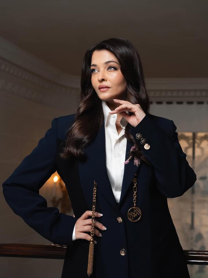 The gold chain accents and medallion detailing serve as standout statement pieces, infusing the look with luxury without overwhelming it. Set against a grand staircase and ornate interiors, the aesthetic radiates power, class, and refined beauty — perfectly encapsulating Aishwarya’s enduring appeal.