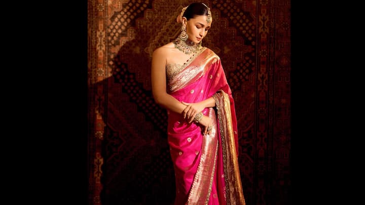 6. आलिया भट्ट: जब परंपरा को ट्रेंड के साथ मिलाने की बात आती है, तो आलिया भट्ट कभी भी पीछे नहीं हटतीं। अभिनेत्री एक सदी पुरानी रेशम की साड़ी में लिपटी हुई अलौकिक लग रही थी, और भारतीय शिल्प कौशल और विरासत का जश्न मना रही थी। जटिल ज़री बॉर्डर के साथ गहरे फ्यूशिया गुलाबी रंग से सराबोर साड़ी, शाही भव्यता को उजागर करती है। सोने के रूपांकनों और विस्तृत शिल्प कौशल ने एक विंटेज आकर्षण प्रदान किया, जबकि आलिया की संतुलित पोशाक और आत्मविश्वासपूर्ण आकर्षण ने आधुनिक अतिसूक्ष्मवाद का स्पर्श लाया। भारी पारंपरिक आभूषणों, एक अलंकृत चोकर, मांग टीका और स्टेटमेंट इयररिंग्स के साथ स्टाइल किया गया आलिया का लुक पुरानी दुनिया की पुरानी यादों और समकालीन ग्लैम का एकदम सही मिश्रण है। (छवि स्रोत: इंस्टाग्राम/@aliaabhatt)