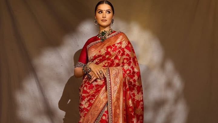 Tara Sutaria looks ethereal in this magnificent red silk saree with intricate gold floral motifs and a lavish border. Styled with a deep red blouse, emerald and pearl jewellery, and a sleek bun, her look radiates heritage luxury and classic Indian elegance. (Image Source: Instagram/ tarasutaria)