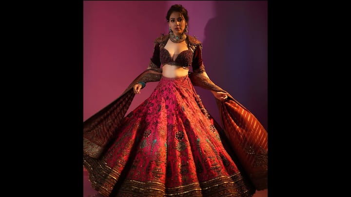 8. रीगल रूबी लहंगा: रंग, सुंदरता और शिल्प कौशल से भरपूर यह लुक एक पूर्ण शोस्टॉपर है। नीति मोहन ने भारी जरदोजी, गोटा और सेक्विन के काम से सराबोर लहंगा पहना था, जिससे यह एक ऐसा परिधान बन गया जो तुरंत ध्यान आकर्षित करता है। विशाल स्कर्ट में गहरे सुनहरे, हरे और वाइन टोन में जटिल पुष्प और पैस्ले रूपांकनों की सुविधा है। इसके साथ रिच वाइन शेड में एक अलंकृत ब्लाउज है, जिसमें गहरी नेकलाइन, संरचित कप और अलंकृत मनके हैं जो अन्यथा पारंपरिक सिल्हूट में एक बोल्ड समकालीन किनारा जोड़ते हैं। पहनावे को पूरा करते हुए, दुपट्टा बुने हुए पैटर्न और धातु विवरण का एक शानदार मिश्रण प्रदर्शित करता है, जिसे इस तरह से लपेटा जाता है कि फ्रेम में गति और नाटकीयता जुड़ जाती है। (छवि स्रोत: इंस्टाग्राम/@नीतिमोहन18)