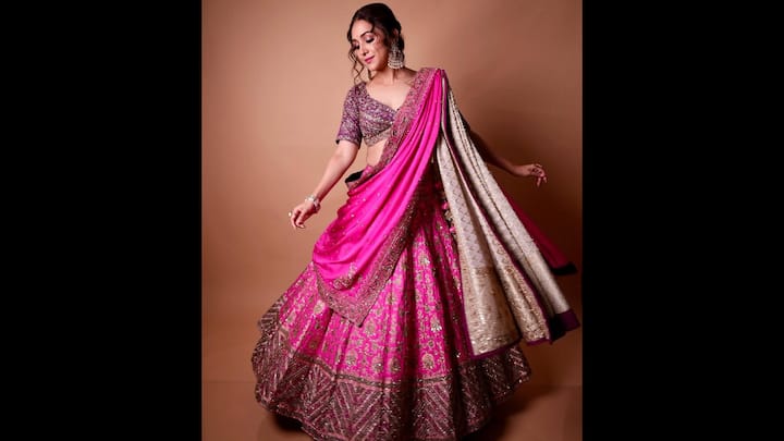 3. हॉट पिंक एम्बेलिश्ड लहंगा: नीति मोहन इस लुभावने हॉट पिंक लहंगे में उत्सव के ग्लैमर को जीवंत कर देती हैं। भारी स्कर्ट में भारी ज़री, सेक्विन और थ्रेडवर्क कढ़ाई है, जो एक शानदार बनावट बनाती है जो खूबसूरती से तस्वीरें खींचती है। उनका ब्लाउज अपनी चमकदार सजावट और गहरी नेकलाइन के साथ एक राजसी आकर्षण जोड़ता है, जो पारंपरिक आकर्षण और आधुनिक आत्मविश्वास के बीच सही संतुलन बनाता है। विषम दुपट्टा, गुलाबी बॉर्डर के साथ एक भव्य हाथी दांत-सोने की बुनाई, आयाम और सुंदरता जोड़ते हुए पूरे पहनावे को एक साथ बांधता है। (छवि स्रोत: इंस्टाग्राम/@नीतिमोहन18)