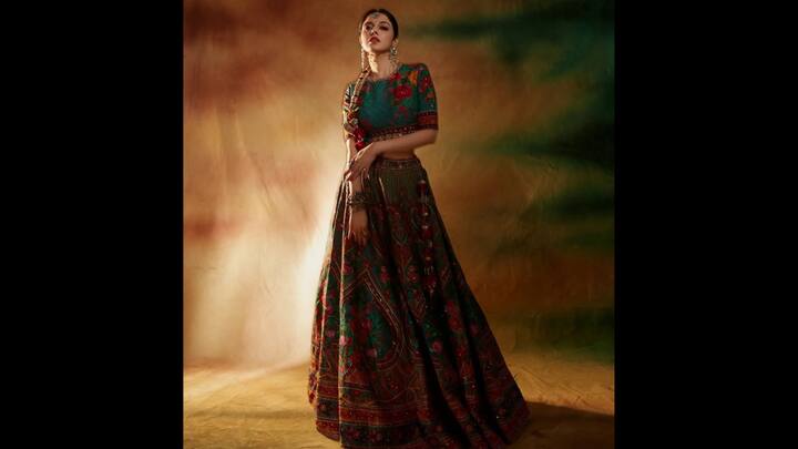6. ⁠Regal Boho Elegance In A Multicoloured Lehenga: If there’s one thing that consistently sets Divya Khosla Kumar apart, it is her ability to turn every ethnic look into a work of art. This outfit  perfectly captures that signature blend of tradition, drama, and cinematic charm. The lehenga stands out with its deep jewel-toned palette, emerald, maroon, rust, and muted gold, woven into intricate floral and heritage folk motifs. The short, fitted blouse echoes the same artisanal embroidery, creating a cohesive yet striking visual balance. The ornate earrings, layered bracelets, and traditional maang-tikka bring in a royal finish, enhancing the festive glamour of the ensemble. (Image Source: Instagram/@divyakhossla)
