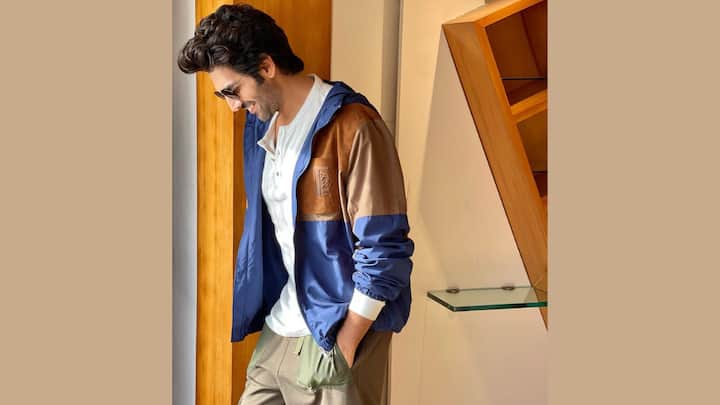 This look blends comfort with earthy charm through a navy, tan and brown colour-blocked windbreaker worn over the white henley. The loose khaki pants with olive pockets add a subtle utilitarian touch, completed with sunglasses and easygoing styling. (Image Source: Instagram/ kartikaaryan)