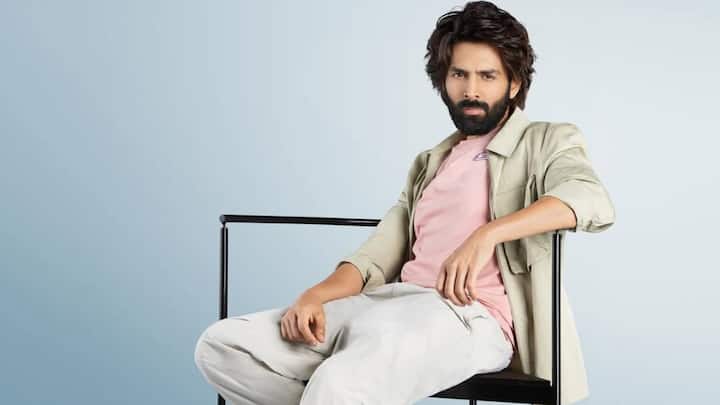 This soft, modern look combines a pink T-shirt with a light beige overshirt and off-white jogger-style pants. White sneakers with teal accents bring a fresh, sporty finish to the neatly coordinated outfit. (Image Source: Instagram/ kartikaaryan)