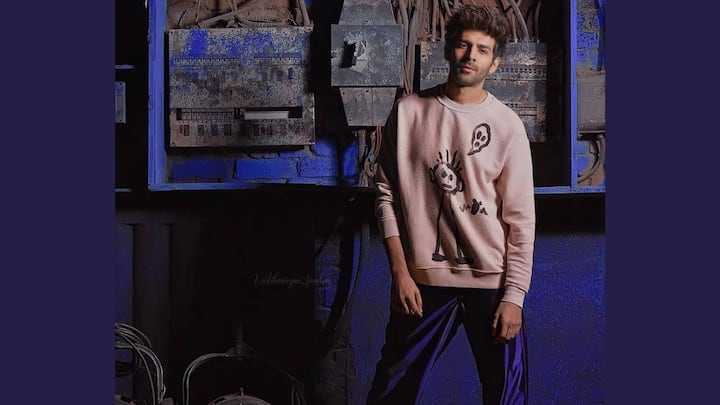 This playful look features a blush-pink graphic sweatshirt teamed with glossy deep-blue track pants for a sporty streetwear vibe. Light sneakers keep the outfit balanced, making it fun, relaxed, and statement-worthy. (Image Source: Instagram/ kartikaaryan)
