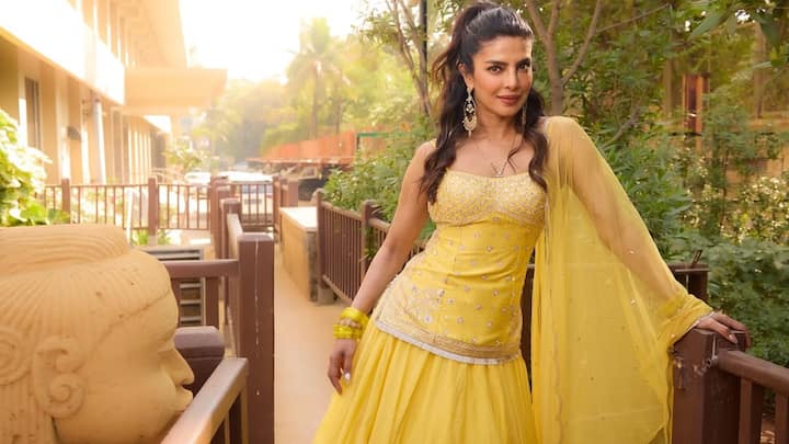Sunshine Yellow Radiance: Priyanka glows in this vibrant sunshine-yellow lehenga crafted from lightweight fabric that moves with effortless grace. The sequin-embellished strapless blouse adds sparkle, balanced by a minimal sheer dupatta. With statement earrings and soft half-up curls, the look feels youthful, bright, and perfect for daytime celebrations. (Image Source: Instagram/ stylebyami)