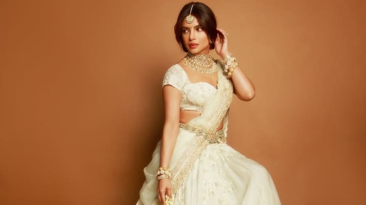 Ivory Elegance: Priyanka radiates soft glamour in this ivory lehenga textured with delicate embroidery and lace, giving the skirt a dreamy, cloud-like flow. The short-sleeved blouse and ornate dupatta add refined detail, while her choker, bracelets, and maang-tikka bring a regal finish. The fresh floral strings in her hand complete the look with a touch of romance. (Image Source: Instagram/ stylebyami)