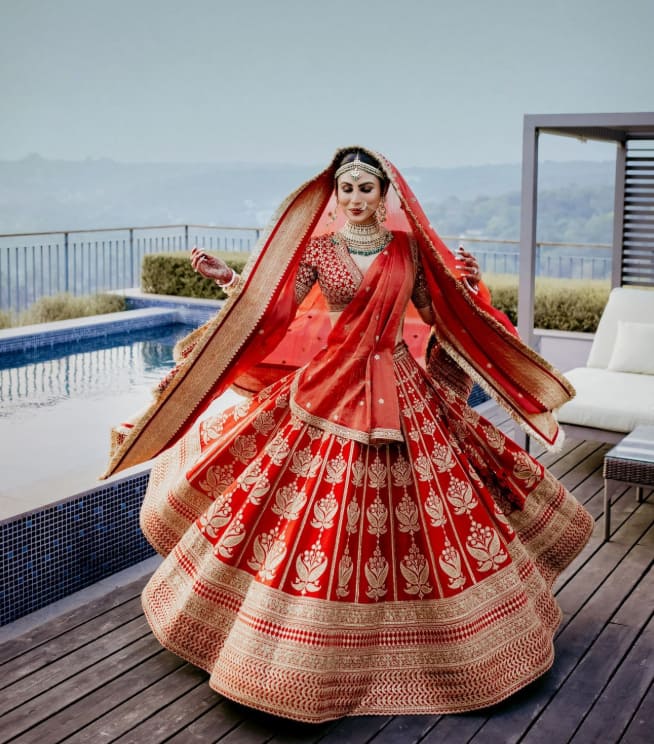 This royal red bridal look of Mouni Roy is the perfect inspiration for the wedding. The heavy golden zari lehenga and double-dupatta drape made her entire look very graceful. Matching jewelery and flawless makeup further enhanced her beauty. If you also want to try something like this on your wedding day, then this style of Mouni can be the best choice for you.