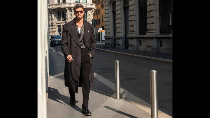 2. Michele Morrone: Stepping out in the heart of Milan, Michele Morrone commands attention in a midnight-black Manish Malhotra trench, satin shirt, and tailored trousers, creating a look that blends European street flair with high-fashion Indian craftsmanship. Draped in a textured tone-on-tone black trench, Morrone channels a blend of mystery and refinement. aired with understated, perfectly cut black trousers, the ensemble feels sleek, powerful, and effortlessly refined. The longline silhouette, structured shoulders, and deep lapels offer a commanding presence, giving the outfit its sharp, cinematic appeal. What truly steals the spotlight is the diamond lion emblem from Manish Malhotra Jewellery, a bold, regal detail pinned to the trench. (Image Source: Instagram/@manishmalhotraworld)