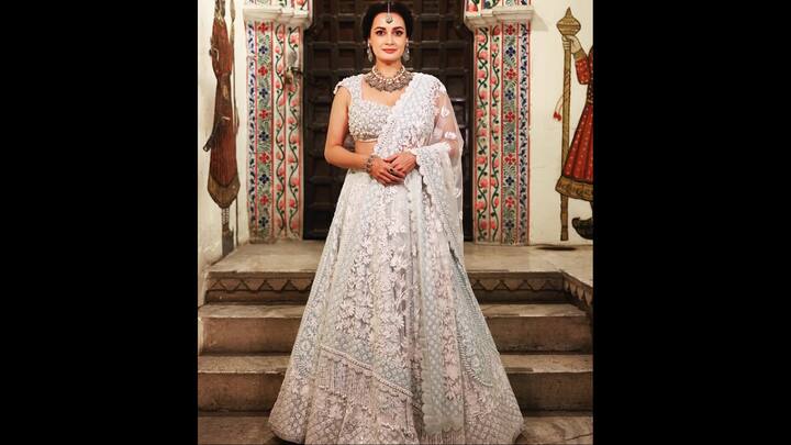 2. White Floral Lehenga: This outfit of Dia Mirza seems like a pure poetry in motion. Dressed in a breathtaking white lehenga, she brings together elegance, nostalgia, and bridal grandeur in a way only she can. The heavily embroidered lehenga features intricate floral work, delicate thread detailing, and shimmering embellishments that catch the light with every movement. The blouse, with its beautifully textured floral pattern, adds depth and dimension. Her sheer dupatta, draped gracefully over one shoulder, highlights the soft, romantic nature of the ensemble. Styled with a stunning kundan choker, statement earrings, and a striking maang tikka, Dia embodies royal Indian bridal glamour. This look is made for every bride who dreams of understated luxury. (Image Source: Instagram/@diamirzaofficial)