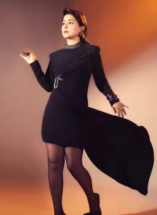 यह आकर्षक काली मिनी ड्रेस ग्लैमर और ग्लैमर का बेहतरीन मेल है। इसकी फिटेड सिलुएट और लहराता हुआ केप इसे शाही लुक देता है। बोल्ड एक्सेसरीज और हील्स के साथ इसे पहनकर आप हिना खान के नए साल की पूर्व संध्या के ग्लैमरस लुक से प्रेरणा ले सकती हैं।