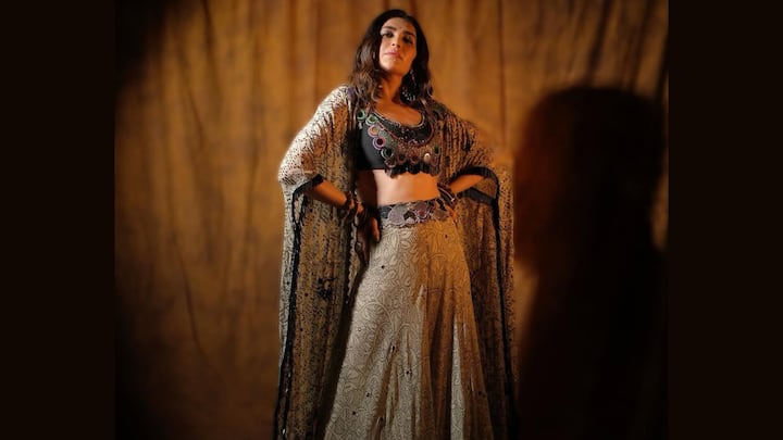 Bohemian Regal Charm: Karishma Tanna embraces ethereal bohemian opulence in this flowing beige lehenga adorned with vintage paisley and floral prints. The mirror-work black blouse and sheer printed cape add artisanal richness, making the look free-spirited yet undeniably regal. (Image Source: Instagram/ karishmaktanna)