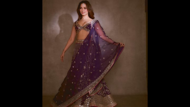 2. Regal Elegance In A Deep Purple Embellished Lehenga Set: Tamannaah Bhatia looks every bit ethereal in this richly detailed purple lehenga ensemble, reaffirming her status as a modern muse for Indian festive and bridal-inspired fashion. The outfit features a heavily embellished lehenga skirt adorned with intricate metallic embroidery and mirror accents that catch the light beautifully, lending the look a luxurious, ceremonial appeal. The deep jewel-toned purple instantly adds royalty to the ensemble, making it a standout choice for weddings, receptions, and grand festive evenings. The structured blouse, designed with ornate detailing and a flattering neckline, perfectly balances tradition with contemporary finesse. Draped gracefully over her shoulder is a sheer dupatta, delicately dotted with subtle embellishments and finished with an ornate border that enhances movement and softness. Styled with minimal yet statement jewellery, including a delicate maang tikka, Tamannaah allows the craftsmanship of the outfit to take centre stage. (Image Source: Instagram/@tamannaahspeaks)