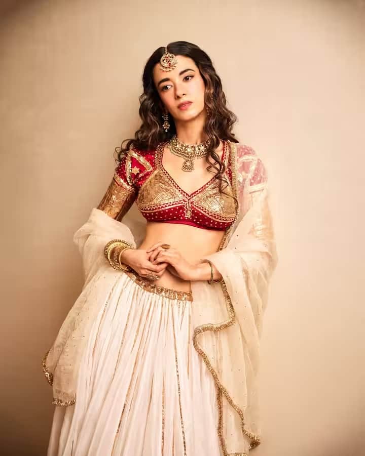 अभिनेत्री ने बॉर्डर पर सुनहरी ज़री की कढ़ाई वाला सफेद लहंगा पहना था। लेकिन सबका ध्यान उनकी डिज़ाइनर ब्लाउज़ पर है। ब्लाउज़ पर भारी कढ़ाई की गई है। यह लाल ब्लाउज़ उनके पूरे पहनावे की खूबसूरती को और बढ़ा रहा है। उन्होंने इसे भारी गहनों के साथ पहना है। हाथों में चूड़ियाँ और माथे पर मांग टीका लगाए वह बेहद खूबसूरत लग रही हैं।