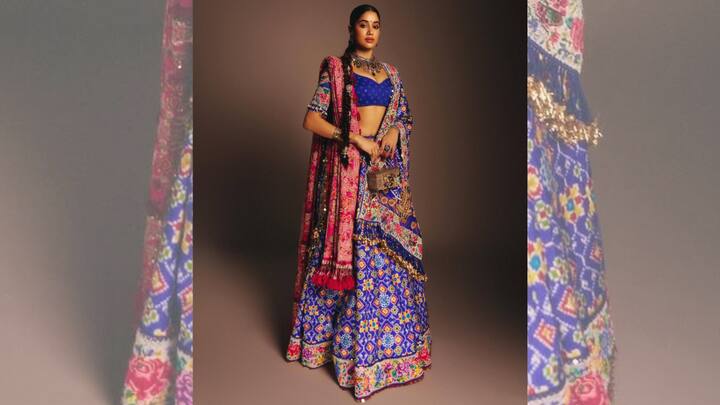 2. Vibrant Royal Blue Lehenga: This striking ethnic look stands out for its bold colours and intricate traditional patterns, making it a true celebration of Indian craftsmanship. The royal blue lehenga instantly grabs attention with its vibrant base, beautifully adorned with multicoloured geometric and floral motifs that reflect rich textile traditions. The detailed patterns across the skirt create a visually dynamic effect. Complementing the skirt is a structured royal blue blouse that keeps the silhouette elegant yet modern. The blouse’s minimal detailing allows the heavily patterned lehenga to remain the focal point while maintaining a balanced and refined aesthetic. Draped effortlessly over the shoulders is a richly embroidered dupatta featuring bold pink and multicolour threadwork, adding another layer of visual drama to the outfit. A statement choker necklace paired with traditional jewellery enhances the regal vibe, while the sleek braid hairstyle adds a touch of timeless elegance. The addition of a small embellished potli bag completes the ensemble with a classic festive accessory that ties the entire look together. (Image Source: Instagram/@janhvikapoor)